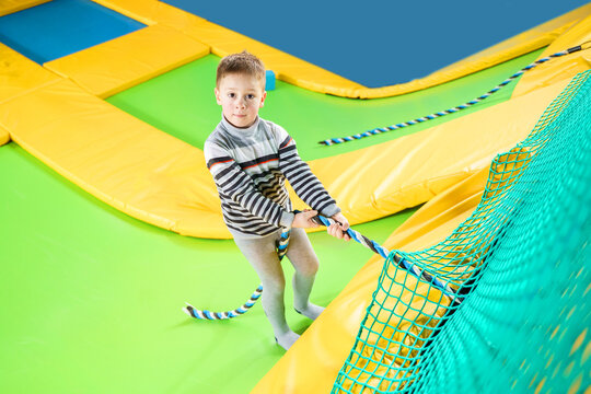 Little boy playing in trampoline center jumping and climbing with rope having fun