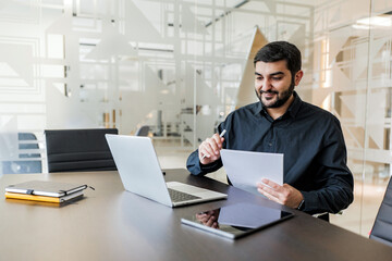 Professional workspace with a focused man reviewing documents and working on his laptop