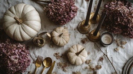 Elegant flat lay with white pumpkins, dried hydrangea flowers, golden cutlery and candles on linen tablecloth. Seasonal autumnal decor and moody Halloween atmosphere