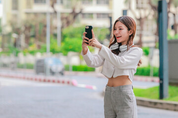 Fototapeta premium Asian Woman Listening to Music and Using Smartphone in Green Urban Setting