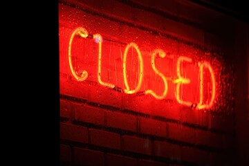 Fototapeta premium Red neon closed sign glowing through rainy window, conveying a somber mood