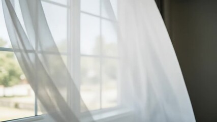 A gentle breeze blows a sheer white curtain in front of a sunlit window. - Powered by Adobe