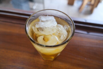 Refreshing glass of cold herbal drink with ice cubes, placed on a wooden surface in natural indoor lighting.
