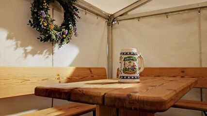 Bright festival tent scene featuring long wooden benches, decorative wreath, and a classic beer stein on the table.
