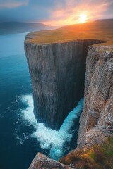 Majestic towering cliff surrounded by blue ocean waves under a vibrant sunset sky with distant hills and a grassy plateau on top