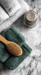 Spa still life soft, white towels, scrub in a glass jar, and a wooden brush atop a teal towel on a marble surface, evoking relaxation and self-care