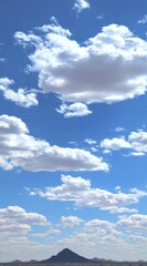 Fototapeta premium Vast blue sky filled with fluffy white cumulus clouds over a distant brown mountainous horizon under bright sunlight