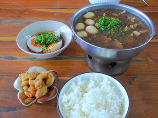 A serving of rice, soup, and fried snacks on a wooden table, styled in muted tones with vintage retro film grain.