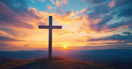 Wooden cross standing on a grassy hilltop overlooking layered mountain ranges during a colorful and dramatic sunset sky