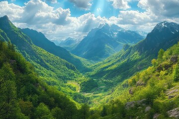Sun rays breaking through clouds over lush green valley surrounded by towering mountains with snow-capped peaks under a partly cloudy blue sky