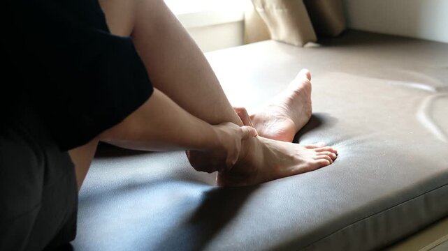 Asian woman&rsquo;s hand holding ankle in pain symbolizing injury, sprain, or joint discomfort