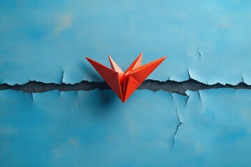 red paper origami bird perched on a cracked blue wall symbolizing resilience and contrast