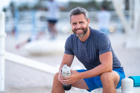 Sport fitness man resting on a bench outdoors. Mature fitness sport model sitting on a bench after a workout. Hispanic sports man taking a break after fitness. Fit guy resting after fitness. - Powered by Adobe