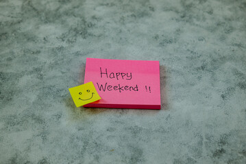 Handwritten words Happy Weekend along with a smile emoji on a piece of pink paper on a bright abstract background. Background