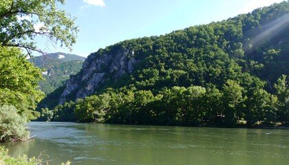 Serene river flows through lush green valley, mountains in background under bright sky