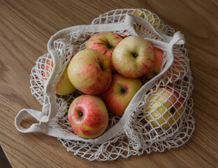 Autumn ripe apples in a string bag on a wooden table