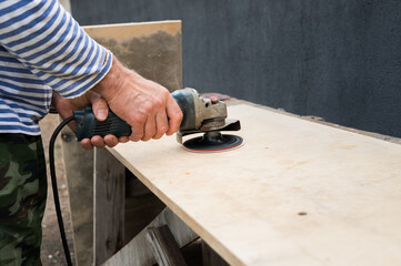 Male carpenter using electric sander on wooden board in workshop
