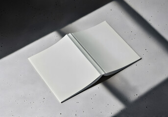 Minimalist shot of an open white book with blank pages on a grey background, illuminated by strong, geometric shadows.