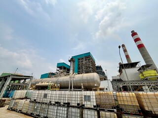 Obraz premium Industrial landscape showing a power plant with storage containers under a cloudy sky highlighting the intersection of energy production and logistical infrastructure in a commercial setting