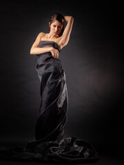 On a dark background is the figure of an attractive woman dressed in a black robe. Her bare...