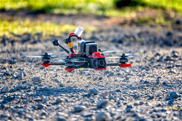 Fpv drone hovering above gravel on a sunny day. The quadcopter is flying a few centimetres from the ground