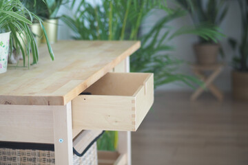 Wooden table with open drawer surrounded by plants indoors