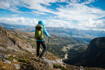 Fototapeta premium Backpacking woman climbing up on steep cliff edge at high altitude mountains top
