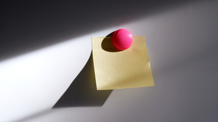 Post it note and pink chalk board magnet on whiteboard with strong shadow. Concept of still-life, abstract, daytime, yellow paper, journey, sticky note for content, poster, cover. Blank post it paper.
