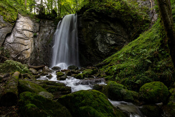 long exposure of a scenic waterfall in a mossy green valley in Switzerland
