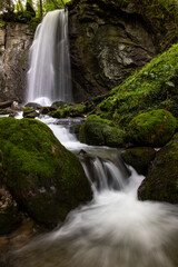 long exposure of a scenic waterfall in a mossy green valley in Switzerland