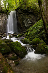 long exposure of a scenic waterfall in a mossy green valley in Switzerland