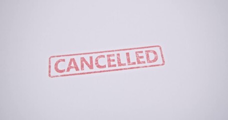 A red ‘CANCELLED’ stamp being pressed onto a white paper document, symbolizing the termination of a contract, rejection of an application, or the official cancellation of an agreement.