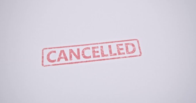 A red &lsquo;CANCELLED&rsquo; stamp being pressed onto a white paper document, symbolizing the termination of a contract, rejection of an application, or the official cancellation of an agreement.