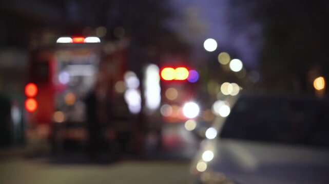 Defocused image of a fire truck flashing emergency lights in an urban setting at night.
