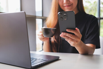 Closeup image of a woman using smart phone and laptop computer while drinking coffee in cafe