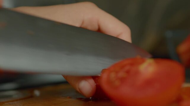 In a cozy kitchen, a woman skillfully chops ripe tomatoes with a knife, preparing fresh ingredients for a flavorful dish. The focus highlights her careful technique.