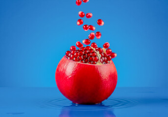 A vibrant closeup of a ripe pomegranate, split open to reveal its juicy red seeds, with a cascade of seeds falling into the blue water, creating ripples on the surface