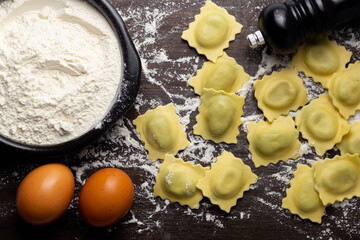 Fresh stuffed ravioli big size on wooden table with flour and eggs