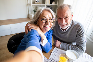 Happy senior couple taking selfie while having breakfast at home