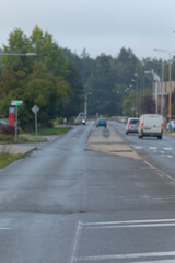 A serene, foggy street view with cars passing by and lush trees lining the road, reflecting tranquility in an urban environment.
