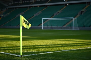 Obraz premium Corner flag stands proudly on the lush green soccer field, bathed in warm sunlight, with goalpost and empty green seats in the background