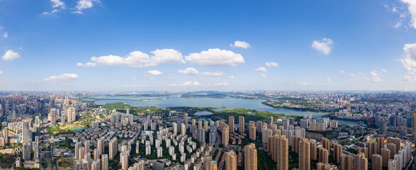 Wuhan, China city skyline stretches across the horizon, showing a vast urban landscape with buildings and a large body of water under a clear blue sky with scattered clouds, panoramic view.
