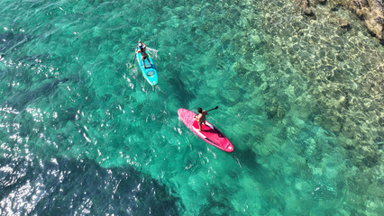 Aerial drone photo of unidentified fit couple practising SUP or Stand Up Paddle surf board in tropical mediterranean clear sea sandy beach