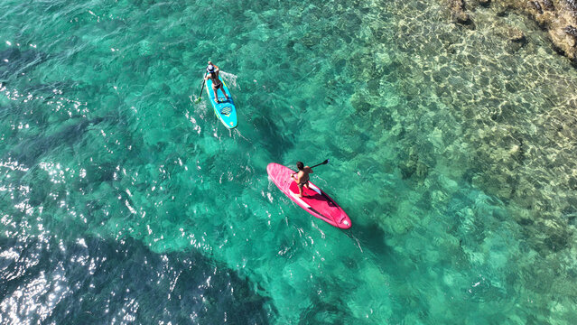 Aerial drone photo of unidentified fit couple practising SUP or Stand Up Paddle surf board in tropical mediterranean clear sea sandy beach