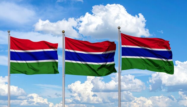 Three Gambian national flags waving in the wind against a bright blue sky with white clouds. - Powered by Adobe