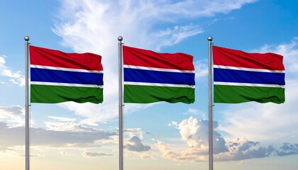 Three Gambian national flags waving in the wind against a bright blue sky with white clouds.
