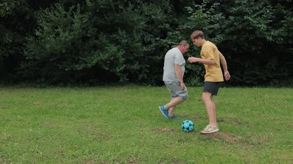 Happy son kicks ball to father, son jumps with joy.Dad and son playing football on the lawn.parent plays with son into ball. - Powered by Adobe