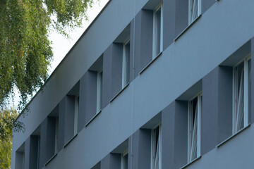 A close-up view of a modern, gray building facade with multiple windows framed by lush greenery, showcasing contemporary architecture.