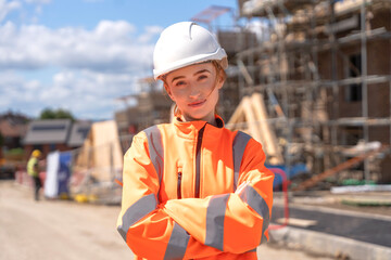 Young female construction worker poses confidently on site with safety gear during a sunny day with...