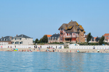 Fototapeta premium Sunny day at Le Crotoy beach in the Bay of Somme with colorful umbrellas, beach huts, and traditional houses by the sea.